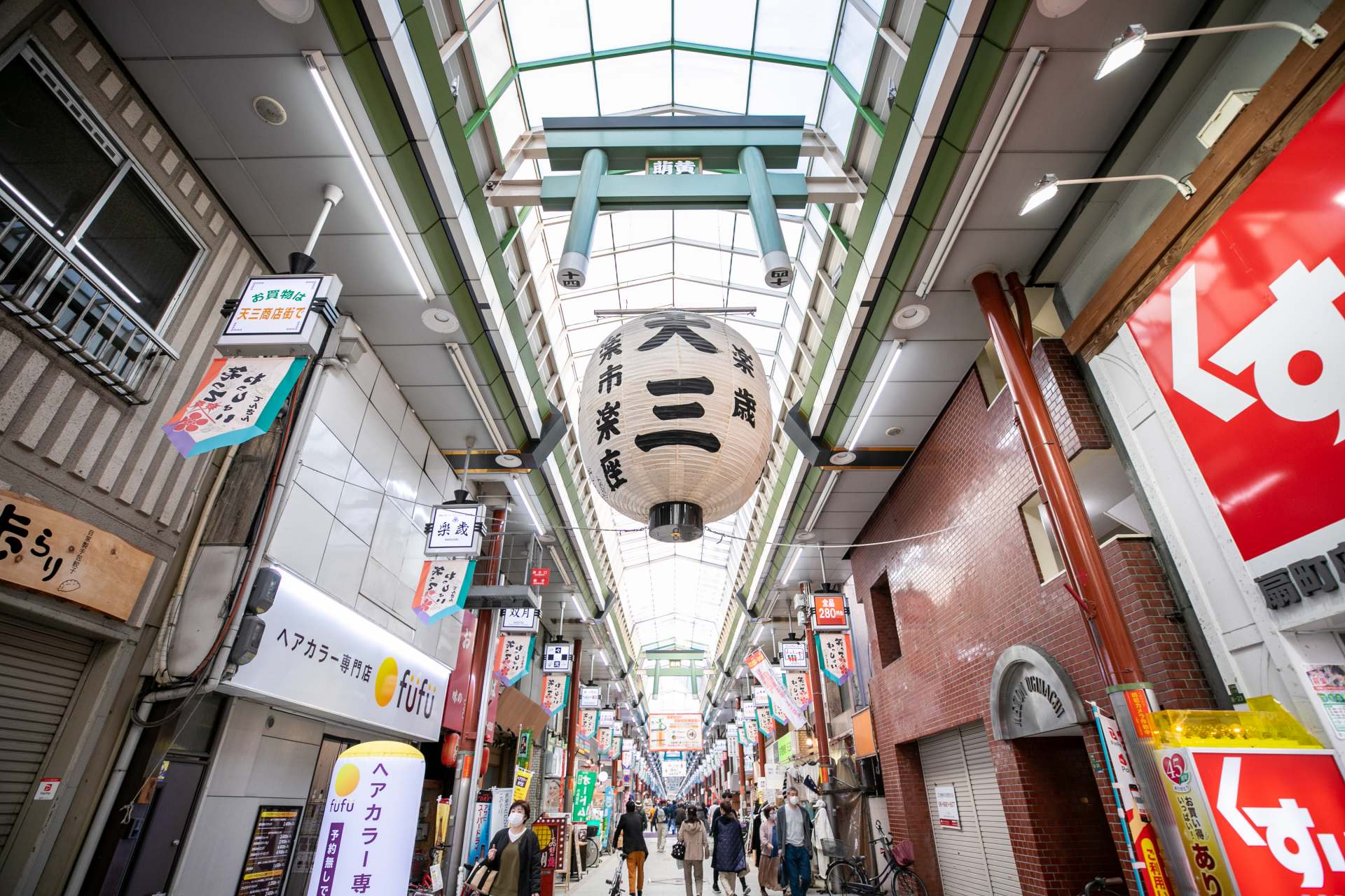 An enclosed arcade design reveals the roots of the street’s prosperity, while the torii gates and lanterns overhead signify the street as the gate to Osaka Temmangu Shrine.