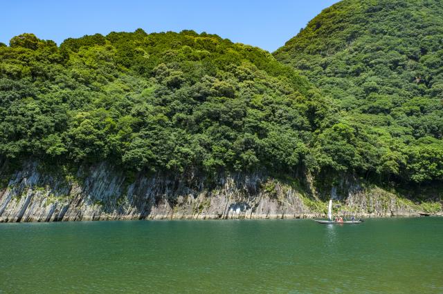 A Sandanbo riverboat sailing on the emerald-green surface of the river with stones as a backdrop